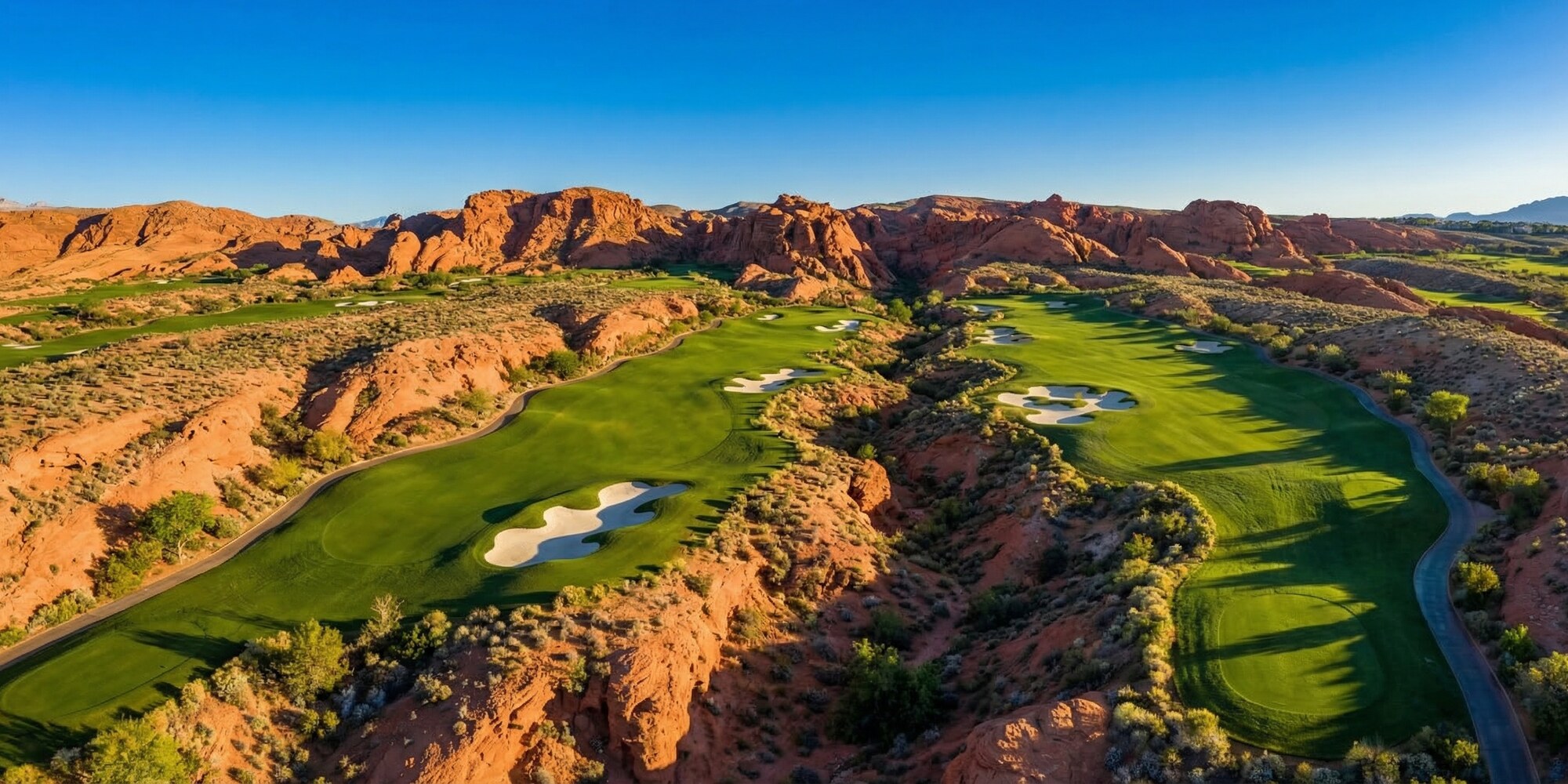 Aerial view of lush Summerlin golf course fairways framed by red rock canyon formations and Nevada desert under a deep blue sky