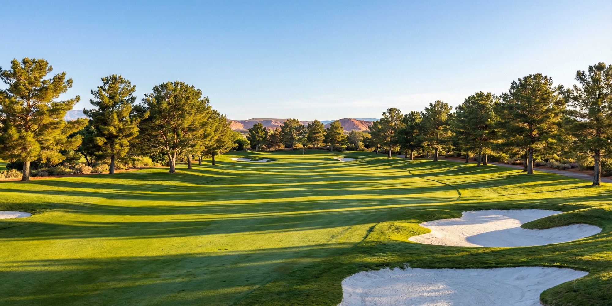 Palm Valley Golf Club fairway lined with mature pine trees at sunrise, white sand bunkers framing manicured Bermuda grass, Nevada desert sky